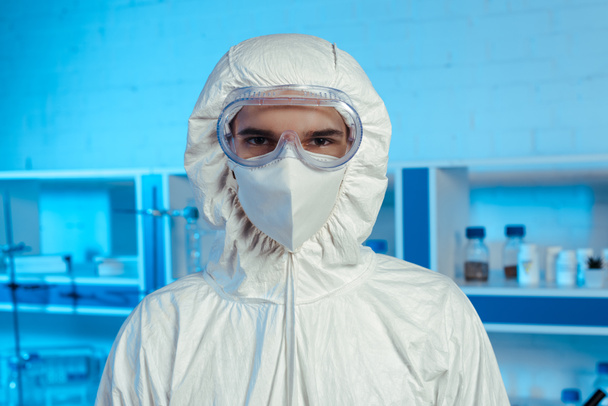 científico en traje de materiales peligrosos, máscara médica y gafas mirando a la cámara
 - Foto, Imagen