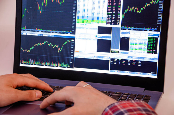 Trading on the exchange. Men's hands in a plaid shirt at a laptop. On-screen rates, promotions. Schedule. Wins are losses. Part of the back and head is visible. Focus on laptop and graphics - Photo, Image