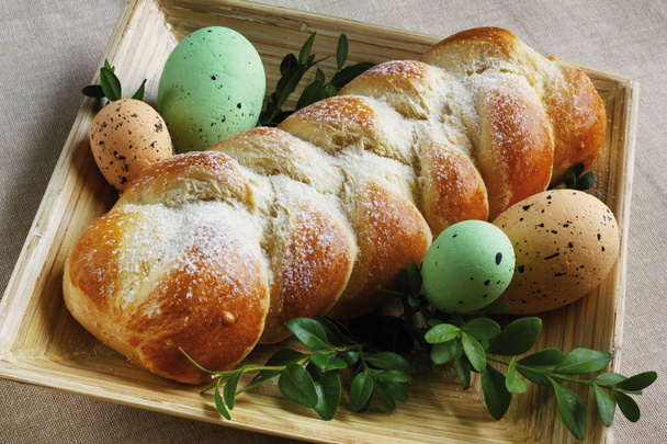 Pan de Pascua casero trenzado dulce con cuatro huevos de Pascua y ramita con hojas decoradas en plato de madera - tiempo de Pascua
 - Foto, Imagen