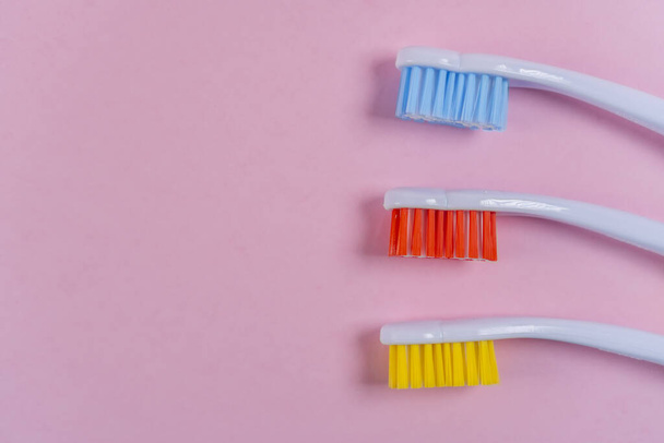 Three colored toothbrushes on a pink background. Red, yellow, blue. Copyspace. Bright tool for dental hygiene - Photo, Image