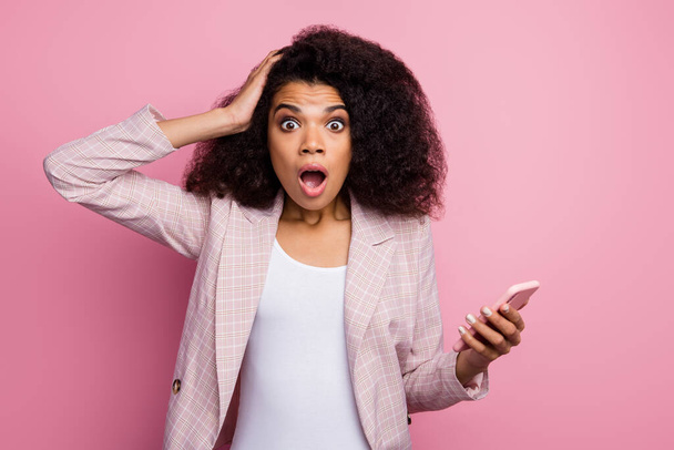 Photo of crazy shocked dark skin lady hold telephone read negative blog post comments open mouth hand on head formalwear checkered blazer isolated pastel color background - Φωτογραφία, εικόνα