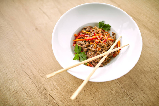 Ανακατέψτε noodles soba με μοσχάρι και chopsticks σε λευκό μπολ, κοντινή θέα - Φωτογραφία, εικόνα