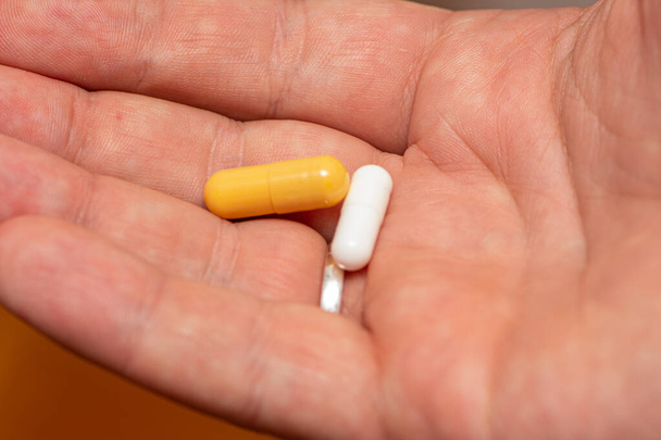 Человек, принимающий две таблетки желтого и белого цвета как лекарство
 - Фото, изображение