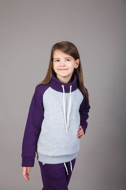 a young girl in sportswear shows it off on a gray background - Foto, imagen