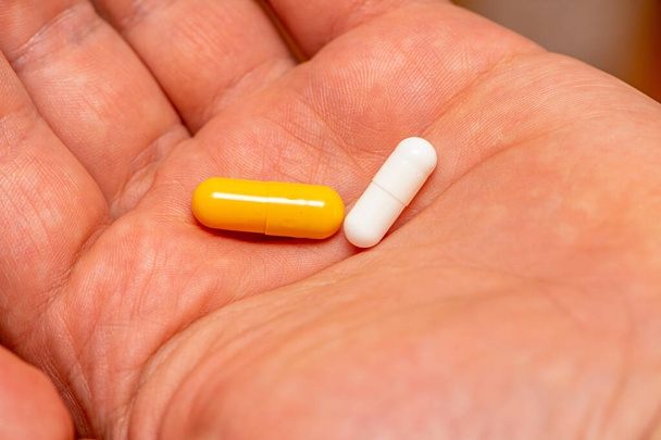 Uomo che prende due pillole gialle e bianche come medicina
 - Foto, immagini