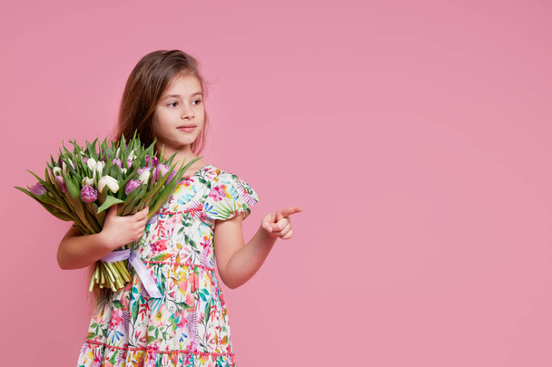 Cute smiling child girl holding bouquet of spring flowers tulips isolated on pink background. Little toddler girl gives a bouquet to mom. Copy space for text.  - Foto, afbeelding