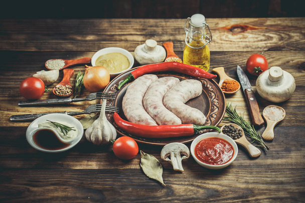 Many different spices, vegetables and ingredients, and fresh raw barbecue sausages for the family. - Zdjęcie, obraz
