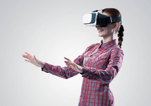 Young woman in checked shirt wearing virtual helmet against gray background - Foto, afbeelding