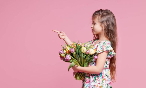 Cute smiling child girl holding bouquet of spring flowers tulips isolated on pink background. Little toddler girl gives a bouquet to mom. Copy space for text.  - Foto, Bild