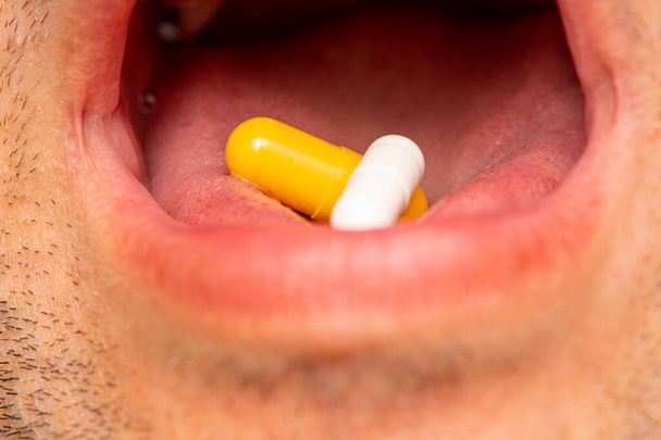 Чоловік приймає дві таблетки жовтим і білим як ліки
 - Фото, зображення