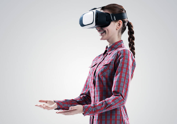 Young woman in checked shirt wearing virtual helmet against gray background - Foto, Bild