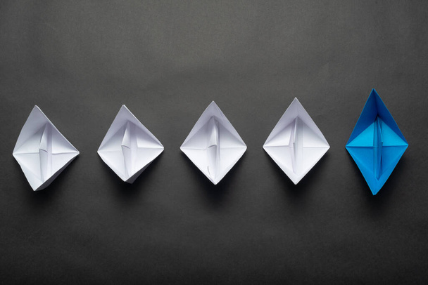 Row of paper ships on black background. Leadership concept with blue paper ship leading among white. Individual motivation and direction. Social marketing layout with copy space. - Foto, Bild