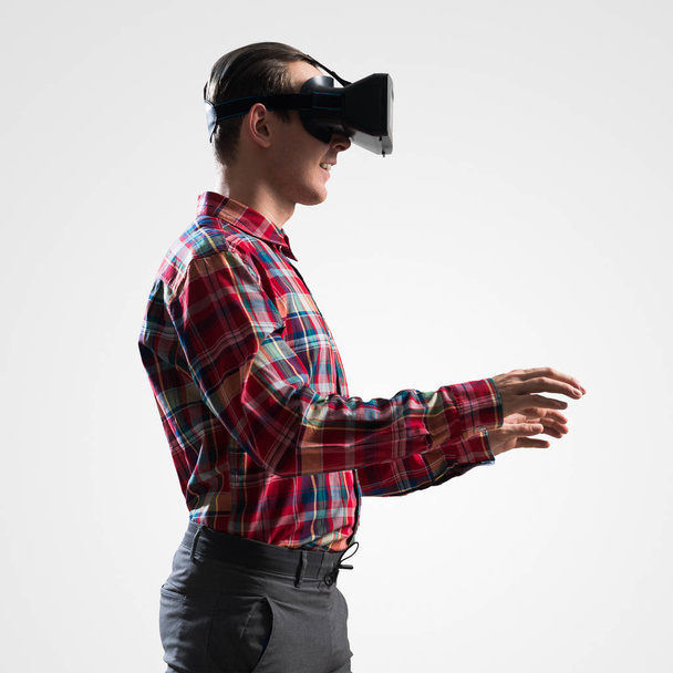 Young man in checked shirt wearing virtual helmet against gray background - Photo, Image