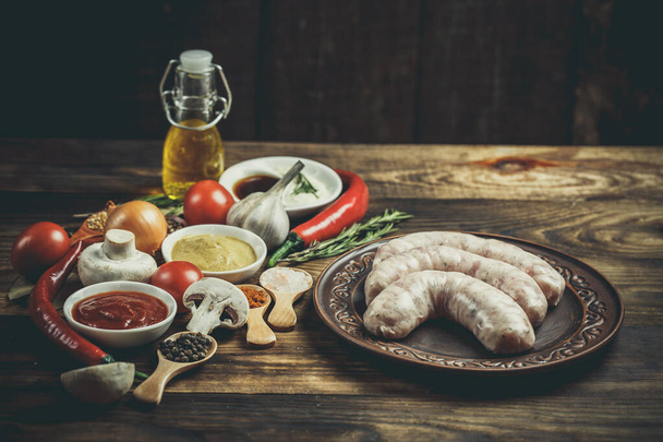 Many different spices, vegetables and ingredients, and fresh raw barbecue sausages for the family. - Zdjęcie, obraz