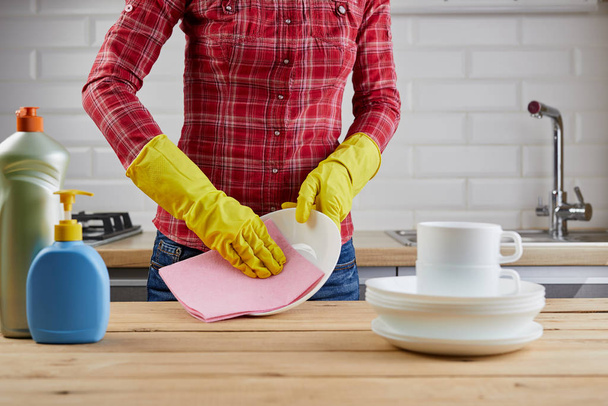The woman in protective glove with white plates, dishes, plastic bottles and cloth, wooden table, kitchen background.Close up. - Foto, Imagem