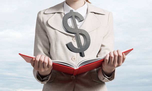 Businesswoman with dollar sign above opened notebook. Investment and money saving services. Close up woman hands holding open book on background of skyscape. Financial company advertising. - Φωτογραφία, εικόνα