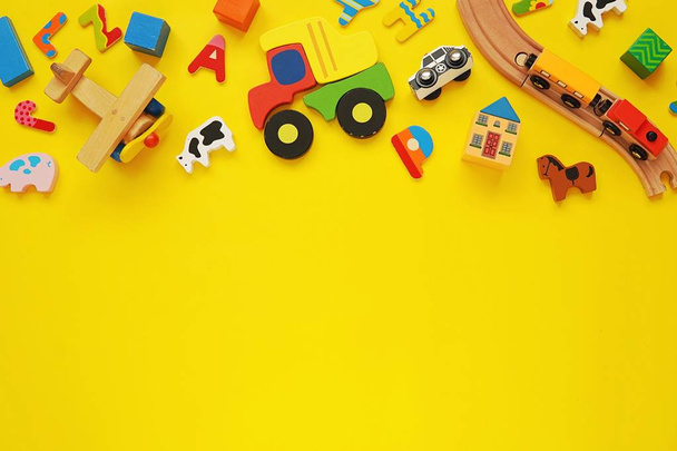 Set of colorful wooden toys for kids, cars, trains, building blocks on yellow background, copy space. - Photo, Image