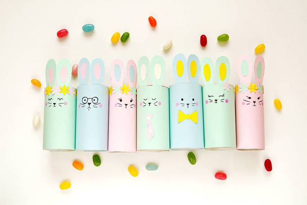 Happy Easter papieren decoraties, schattige konijntjes gemaakt van wc-papier roll, platte lay compositie met kleurrijke snoepjes, eenvoudige ambachten voor kinderen. - Foto, afbeelding