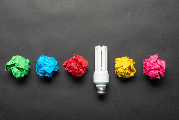 Fluorescent lamp and crumpled colorful paper balls on black background. Successful solution of problem. Idea generation and brainstorming motivation. Great idea among failing ideas metaphor. - Photo, Image