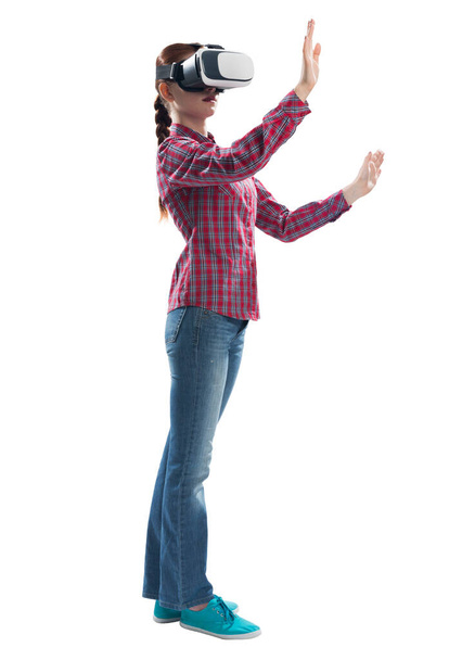Young woman exploring virtual world, interacting with digital interface. Lady wearing VR goggles and gesturing in air. Studio photo by side view girl against gray background. Cyber technology concept - Foto, Bild