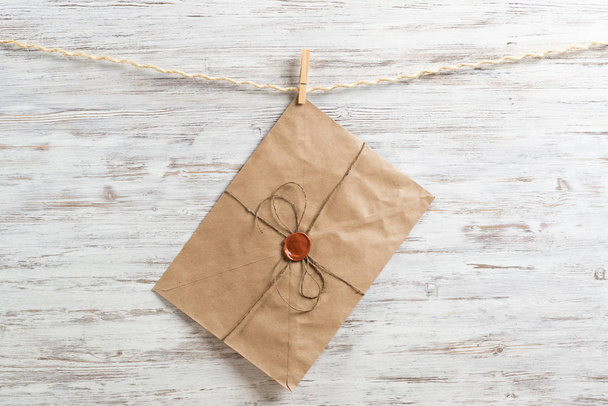 Old paper envelope hanging on rope on wooden background. Twine rope with wooden clothespins. Brown letter envelope with wax seal stamp. Retro communication and correspondence. Delivery service layout - Фото, изображение