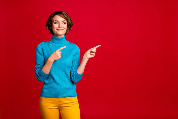 Portrait of positive cheerful girl promoter point index finger look copyspace indicate ads promotion recommend direct way wear stylish clothes isolated over red color background - 写真・画像