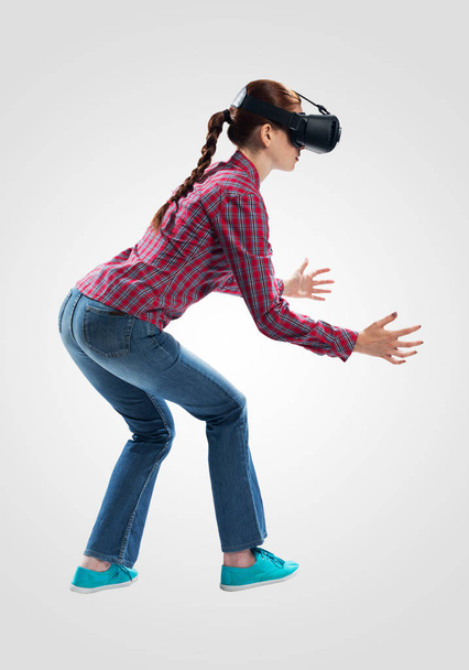 Young woman wearing VR headset and gesturing in air. Lady something lifts up or down. Interacts with cyberspace using gestures. Studio photo by girl against gray background. Virtual reality simulation - Fotoğraf, Görsel