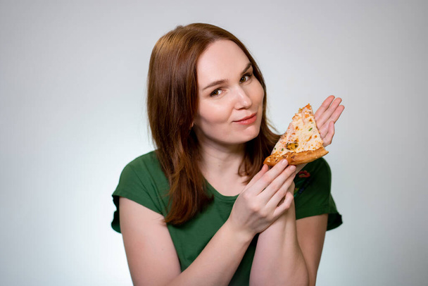 A woman brown hair holding piece of pizza, laughs - Zdjęcie, obraz