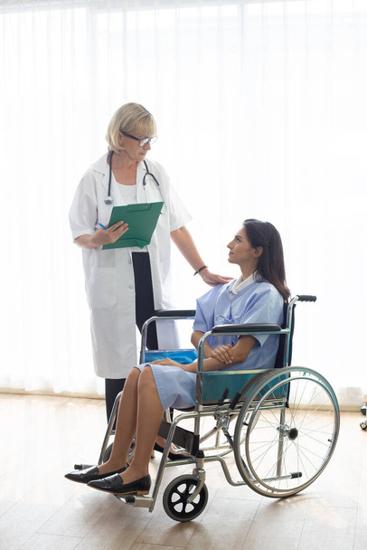 Orvos és türelmes nő ül tolószéken megvitatása valamit egészségügyi szobában kórház, egészségügyi koncepció. - Fotó, kép