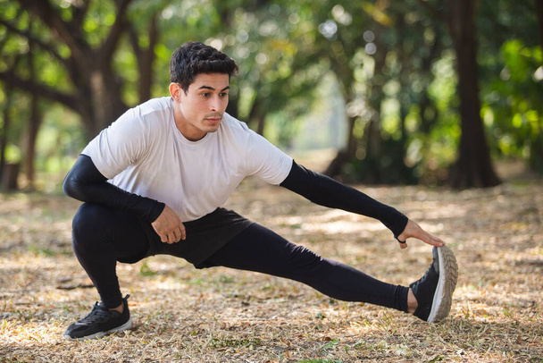 Man in sportswear performs stretching warm up before exercise  in public park. - Photo, Image