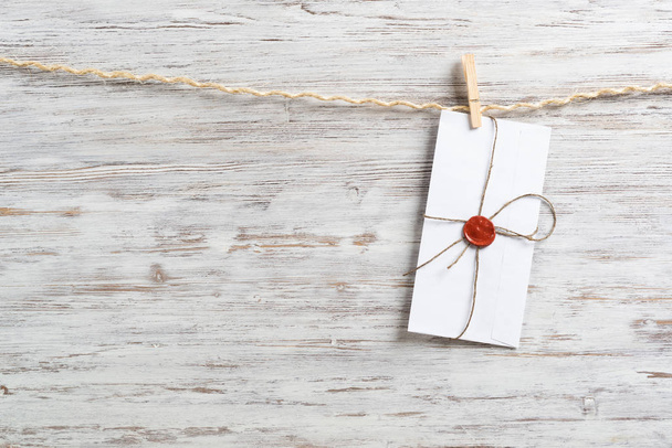 White classic envelope hanging on twine rope with clothespins. Vintage declaration of love on wooden painted background. Retro letter envelope with sealing wax stamp. Romantic wedding invitation. - Φωτογραφία, εικόνα