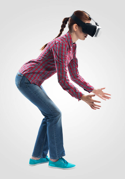 Young woman wearing VR headset and gesturing in air. Lady something lifts up or down. Interacts with cyberspace using gestures. Studio photo by girl against gray background. Virtual reality simulation - Foto, Imagem