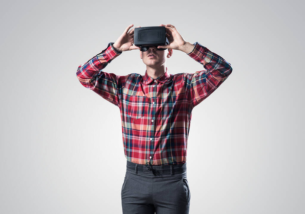Young man in checked shirt wearing virtual helmet against gray background - Photo, Image