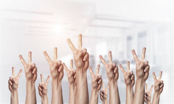 Row of man hands showing victory gesture. Winning or triumph group of signs. Human hands gesturing on light blurred background. Many arms raised together and present popular gesture. - Photo, Image