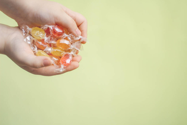 multi-colored candy caramel in the hands of a child on a light yellow background. concept of sweets and rewards for children - 写真・画像
