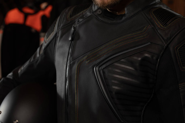 Чоловік у шкіряній куртці тримає мотоциклетний шолом
 - Фото, зображення