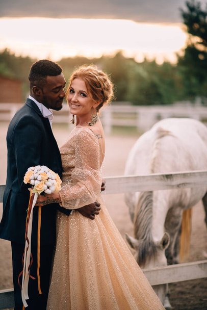 Happy smiling newlyweds standing on ranch surrounded by horses. - Фото, зображення