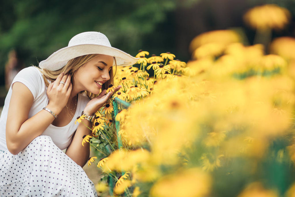 Mooie jonge vrouw ruiken gele bloem in het park. - Foto, afbeelding