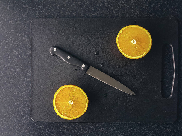 Σύνθεση κομμένου πορτοκαλιού και μαχαιριού σε μαύρο ξύλο κοπής. - Φωτογραφία, εικόνα