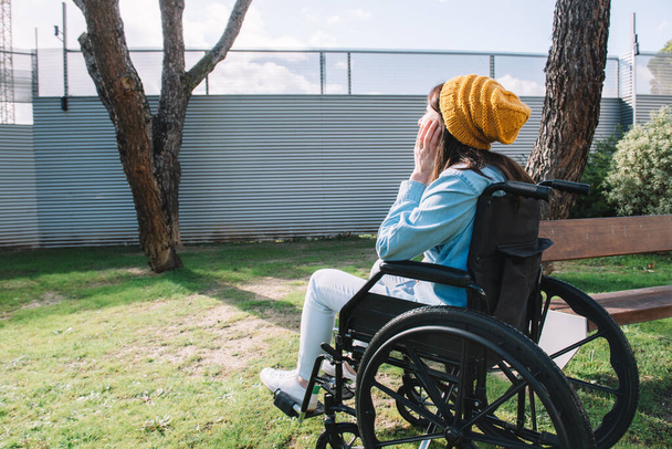Девушка-инвалид в инвалидной коляске в саду наслаждается солнечным днем
 - Фото, изображение