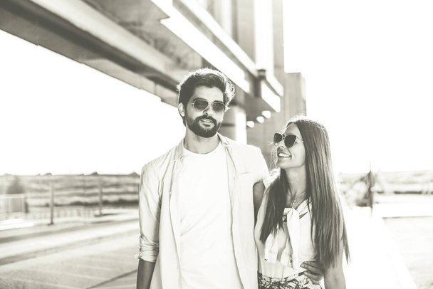 A young couple walks in a hug. They are stylishly dressed and wear sunglasses. Black and white photo. - Photo, Image