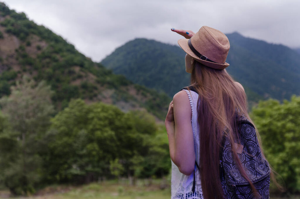 Νεαρή τουρίστρια με ψάθινο καπέλο κοιτάζει την απόσταση στη φύση. πίσω όψη. Έννοια ταξιδιού μόνος. - Φωτογραφία, εικόνα