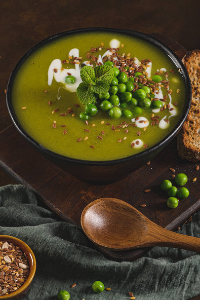 Green pea soup with linseed and pumpkin and sunflower seeds on a rustic kitchen countertop. - Foto, Imagem
