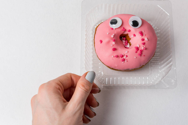 Frauenhand und lustiger Donut mit großen Augen in Plastikbehältern. ökologisches Konzept. - Foto, Bild
