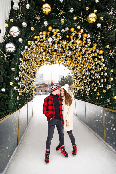 beautiful young couple of lovers standing on ice rink and decorated Christmas tree background - Photo, image