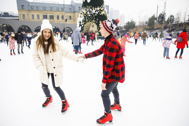 young couple of lovers in winter clothes and red skates skating on city skating rink background - Fotó, kép