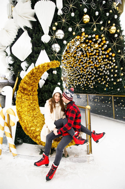 happy and young couple siting on ice rink and decorated Christmas tree background - Photo, Image