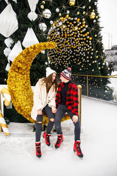 beautiful and young couple of lovers posing on ice rink and decorated Christmas tree background - Fotoğraf, Görsel