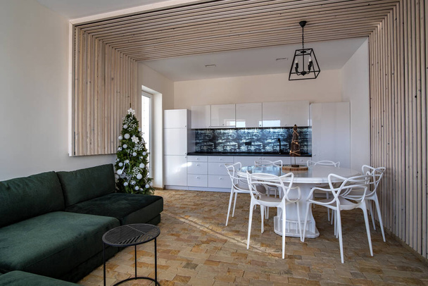 Interiér moderní prostorné kuchyně s bílými stěnami, dekorativními dřevěnými prvky, moderním nábytkem a velkým měkkým gaučem. - Fotografie, Obrázek