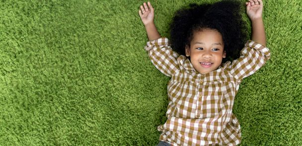 Happy children little girl smiling and laying on green carpet floor in living room at home. - Fotó, kép